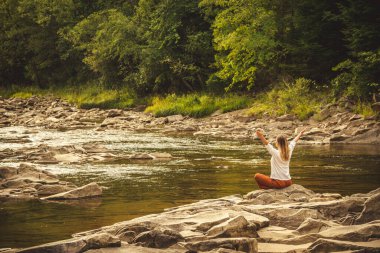 Woman doing yoga on the green grass on the top of the mountain with beautiful view at sunset