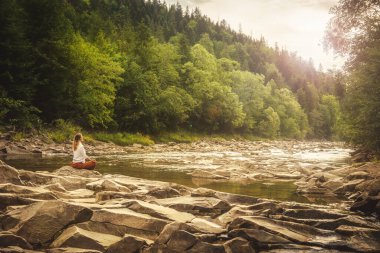 Dağın tepesindeki yeşil çimlerde yoga yapan kadın gün batımında güzel manzaralı.