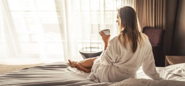 Young woman with bathrobe have a Breakfast in bed, cozy hotel room.