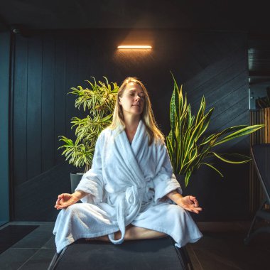 Woman in white bathrobe lying on sofa and relaxing with at home near window