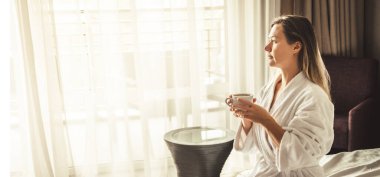 Woman in white bathrobe lying on sofa and relaxing with orange cocktail at the roof of hotel