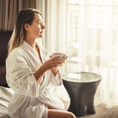 Woman in white bathrobe lying on sofa and relaxing with orange cocktail at the roof of hotel