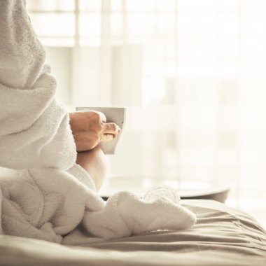 Woman in white bathrobe and towel lying on sofa and relaxing with tea at the roof of hotel
