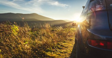 Dağ yolunda seyahat etmek için bir araba. Mavi gökyüzü ve güneş