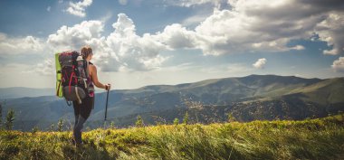Sırt çantalı genç bir kadın dağda yürüyüş yapıyor.