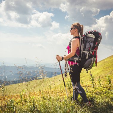 Sırt çantalı genç bir kadın dağda yürüyüş yapıyor.