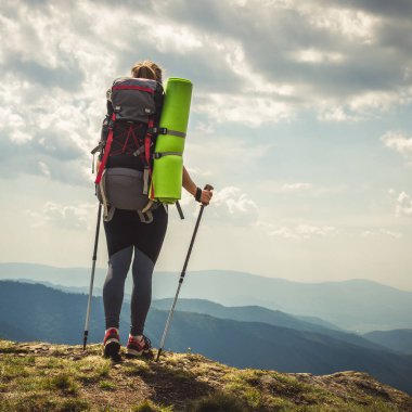 Sırt çantalı genç bir kadın dağda yürüyüş yapıyor.