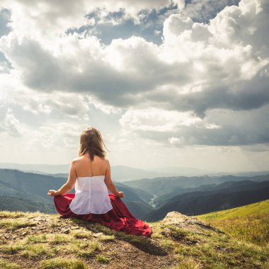 Genç bayan dağın tepesinde meditasyon yapıyor kırmızı elbiseli.