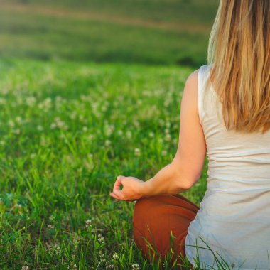 Dağın tepesindeki yeşil çimlerde yoga yapan kadın gün batımında güzel manzaralı.
