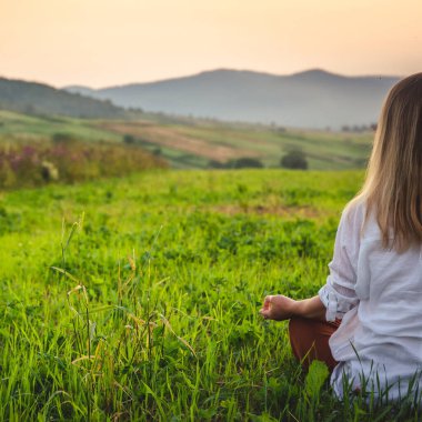 Dağın tepesindeki yeşil çimlerde yoga yapan kadın gün batımında güzel manzaralı.