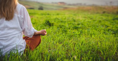 Dağın tepesindeki yeşil çimlerde yoga yapan kadın gün batımında güzel manzaralı.