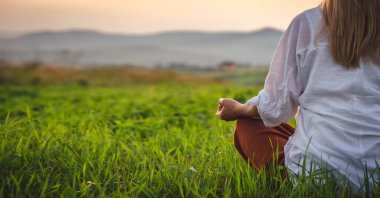 Dağın tepesindeki yeşil çimlerde yoga yapan kadın gün batımında güzel manzaralı.