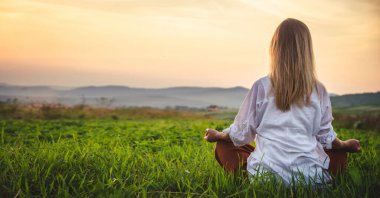 Dağın tepesindeki yeşil çimlerde yoga yapan kadın gün batımında güzel manzaralı.