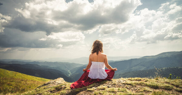 Young woman meditate on the top of mountain in red dress