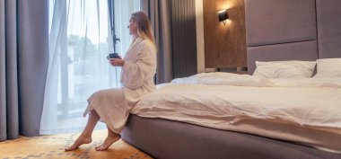 Woman in white bathrobe lying on sofa and relaxing with orange cocktail at the roof of hotel