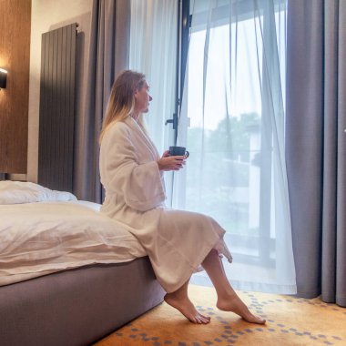 Woman in white bathrobe lying on sofa and relaxing with orange cocktail at the roof of hotel