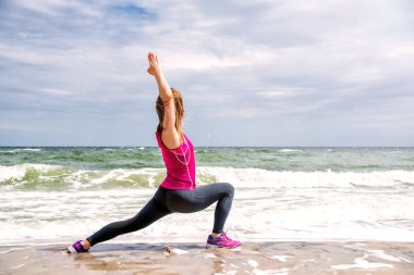 Gün batımında kumsalda yoga yapan bir kadın. Kollarını ve bacaklarını uzatan bir kadının silüeti.