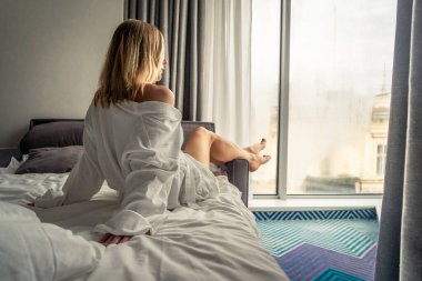 Beyaz bornozlu kadın kanepede uzanıyor ve pencerenin yanında dinleniyor.