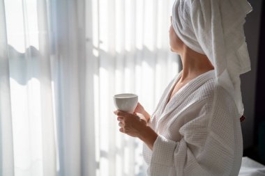 Sabahları bornozlu bir kadın ve bir fincan kahve.