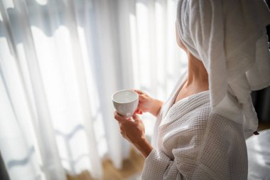 Sabahları bornozlu bir kadın ve bir fincan kahve.