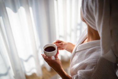 Sabahları bornozlu bir kadın ve bir fincan kahve.