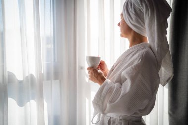 Sabahları bornozlu bir kadın ve bir fincan kahve.