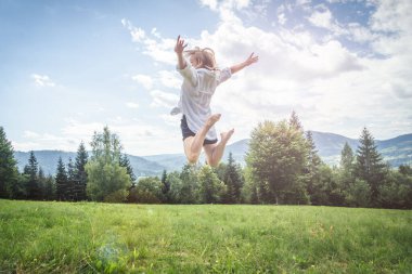 Dağlardaki çayırlarda zıplayan mutlu genç kadın. Özgürlük kavramı.