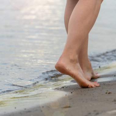 Kumsalda yürüyen bir kadın kumların üzerinde ayak izleri bırakıyor.