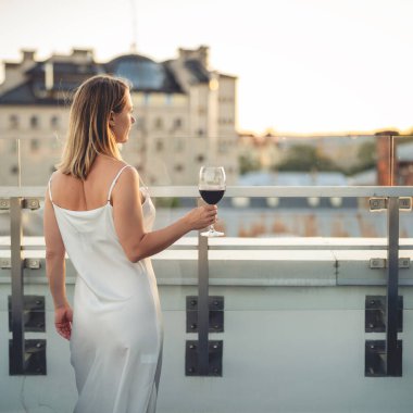 Şatafatlı kadın elinde bir bardak şarap tutarak şehri seyrediyor. Tatillerde seksi beyaz elbiseler giyen zarif bir bayan..