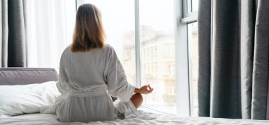 Woman in white bathrobe lying on sofa and relaxing with at home near window