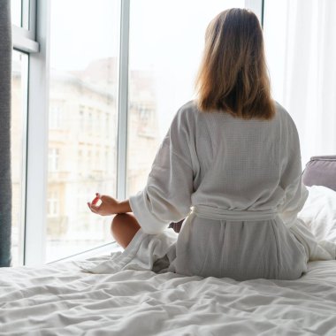 Woman in white bathrobe lying on sofa and relaxing with at home near window