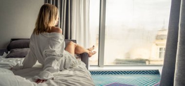 Beyaz bornozlu kadın kanepede uzanıyor ve pencerenin yanında dinleniyor.