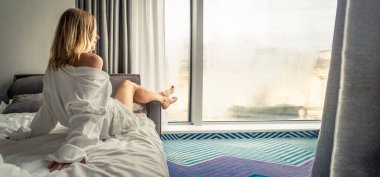 Beyaz bornozlu kadın kanepede uzanıyor ve pencerenin yanında dinleniyor.