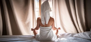 Havluyla yatakta oturup meditasyon yapan genç bir kadın.