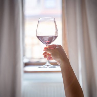 Pencerenin önünde kırmızı şarap bardağını tutan bir kadın. Otel