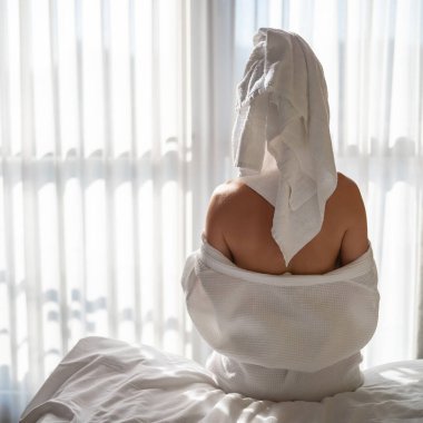 Kafasında havlu olan bir kadın sabah otel odasında oturuyor.