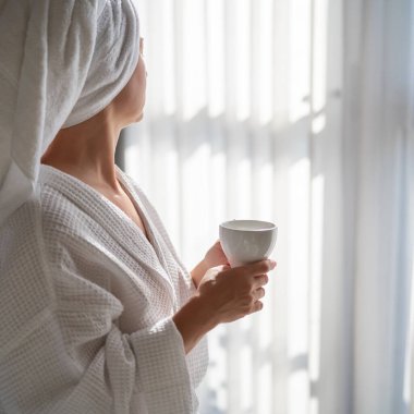 Sabahları bornozlu bir kadın ve bir fincan kahve.
