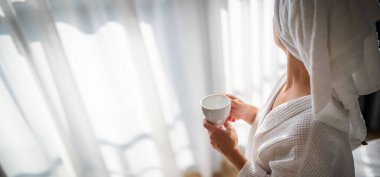 Sabahları bornozlu bir kadın ve bir fincan kahve.