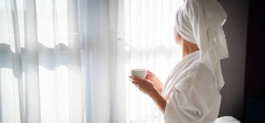 Sabahları bornozlu bir kadın ve bir fincan kahve.