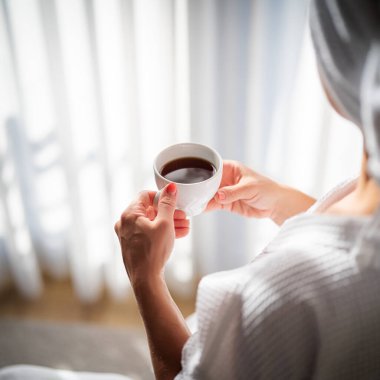 Sabahları bornozlu bir kadın ve bir fincan kahve.