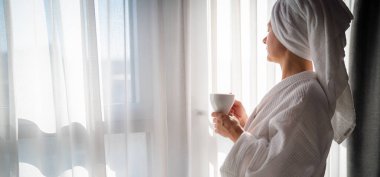 Sabahları bornozlu bir kadın ve bir fincan kahve.