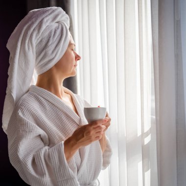 Sabahları bornozlu bir kadın ve bir fincan kahve.