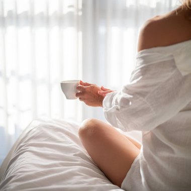 Sabahları elinde kahve olan bir kadın oteldeki battaniyenin altında.
