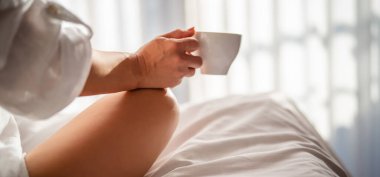 Sabahları elinde kahve olan bir kadın oteldeki battaniyenin altında.