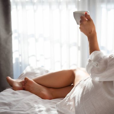 Bornozlu genç bir kadın. Yatakta oturuyor ve otelde kahve içiyor.