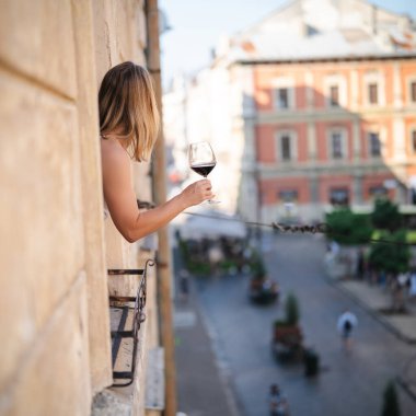 Lviv 'in balkonunda elinde bir kadeh kırmızı şarap olan genç bir kadın.