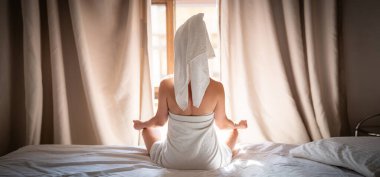 Havluyla yatakta oturup meditasyon yapan genç bir kadın.