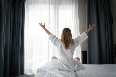 Woman in white bathrobe lying on sofa and relaxing with at home near window