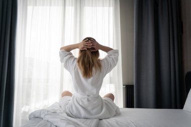 Woman in white bathrobe lying on sofa and relaxing with at home near window