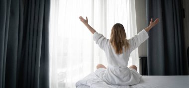 Woman in white bathrobe lying on sofa and relaxing with at home near window